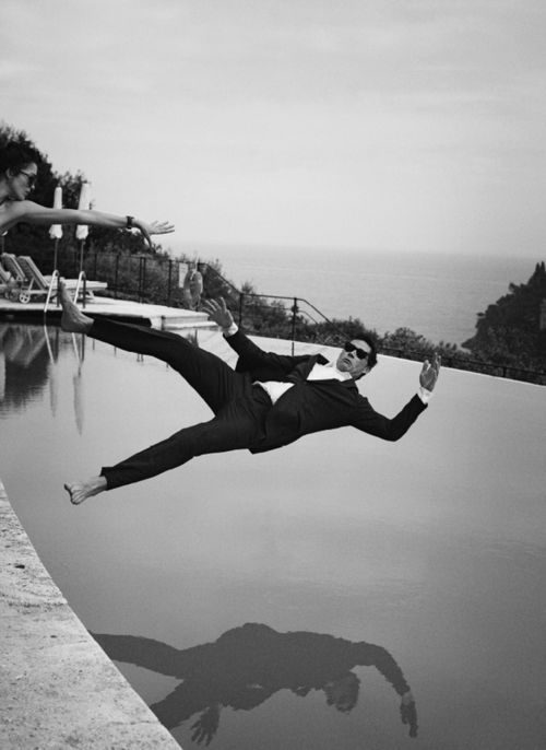 A guest in black tie mid-air above still water, the sea behind