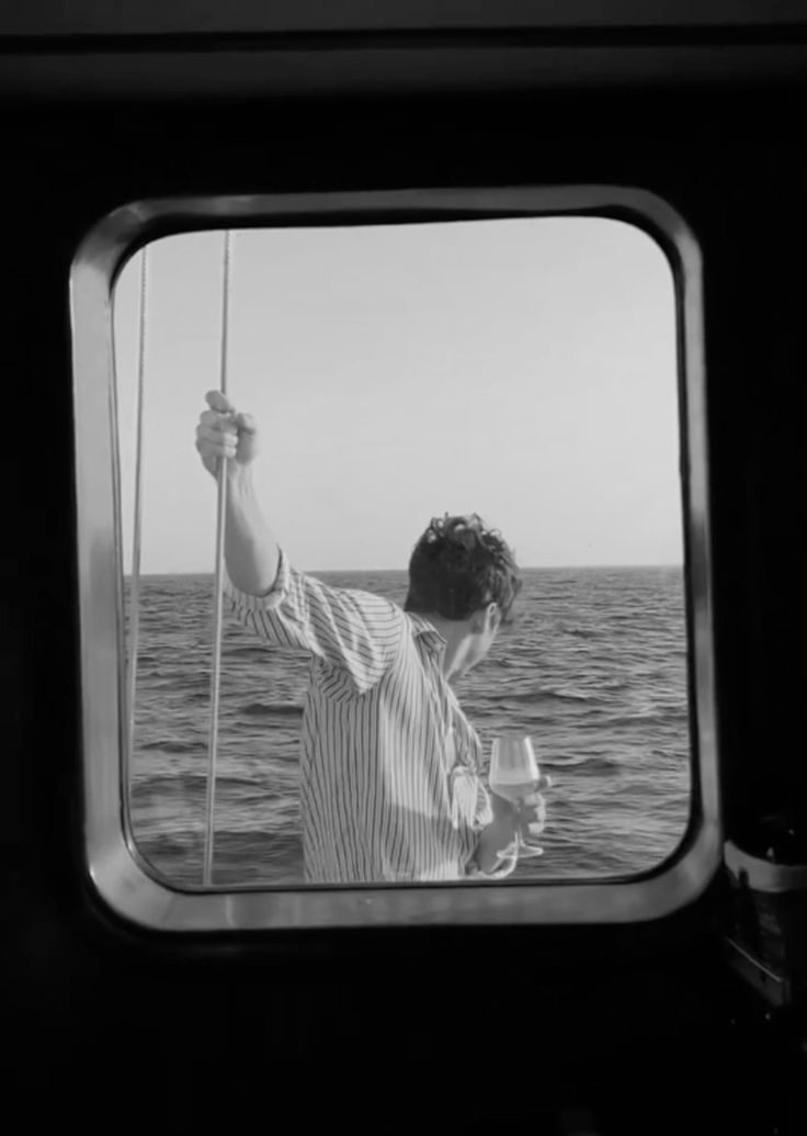 Seen through a porthole: a guest at the rail with a glass in hand, open water beyond